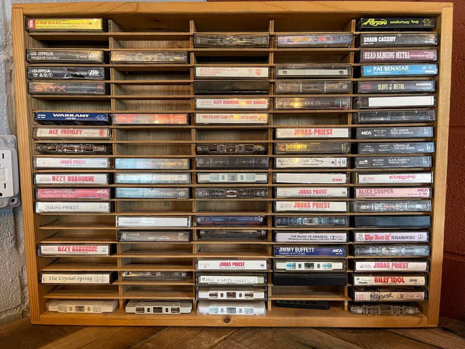 A wooden rack of cassette tapes—titles include selections by Ozzy Osbourne, Judas Priest, Warrant, Europe, and The Escape Club. Also some Mozart and Tchaikovsky for good measure.